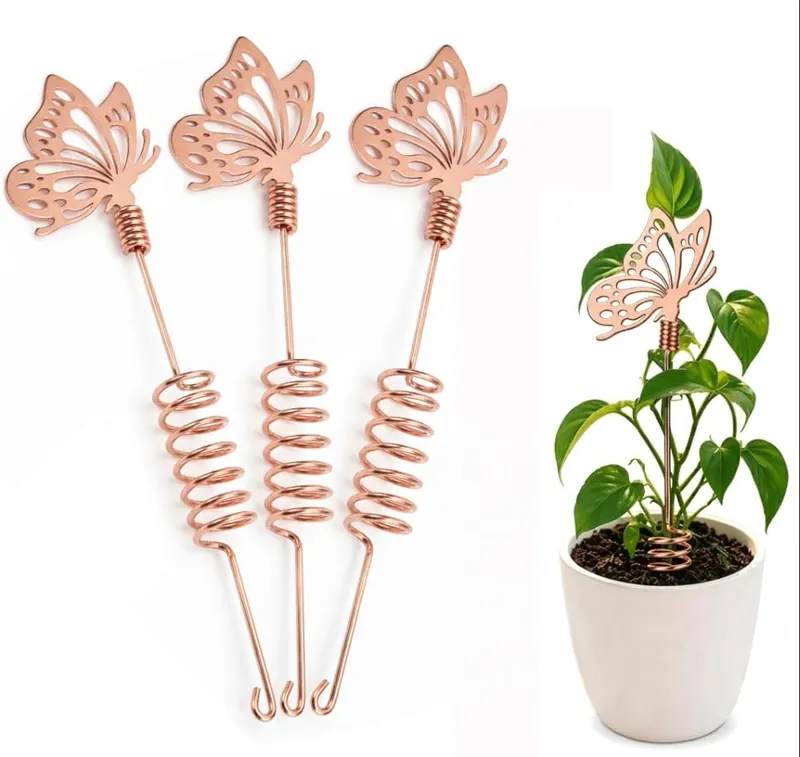 Three copper butterfly garden stakes with coiled stems on a white background, and one of them standing in a white pot beside a pothos plant