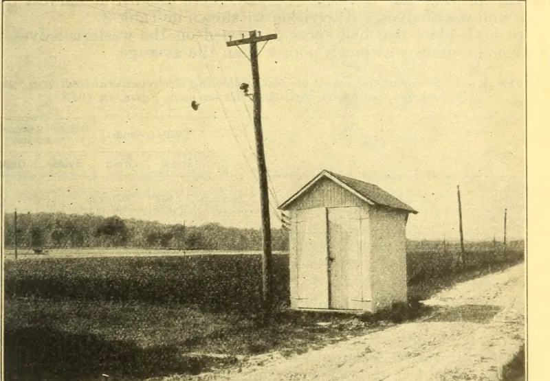 USDA photograph of the Arlington Experiment Farm electroculture plots: a tall pole carrying insulators and wires next to a small gabled apparatus shed by a dirt road